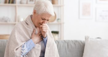 Sick senior woman covered in blanket and coughing